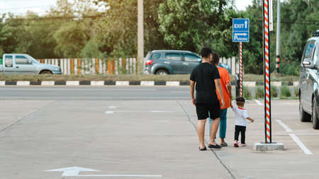 Back view of Asian family on the way back to car parking lot. Parents take care and hold their young...