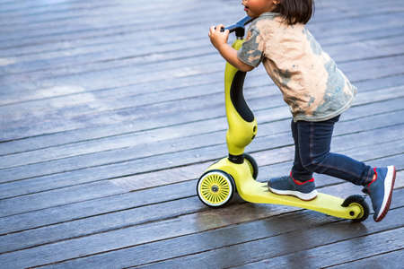 Asian kid enjoy playing and riding scooter without using any safety gear in home. Active lifestyle of children in nature. Happy little boy ride scooter without helmet. Active sport for preschool kid.の写真素材
