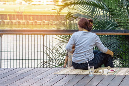 Back view of Asian mother and child relax and chilling with beverage at riverside. Relax lifestyle for family enjoying freedom together in summer holidays. Happy people outdoor resting at waterfront.の写真素材
