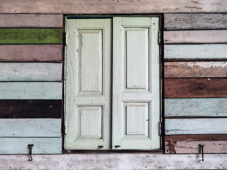 Old grunged wooden window frame painted white vintage with old colourful plywood wall. Antique window frame and old panes. Old closed window and planks of old wooden house. Background of wooden wallsの写真素材