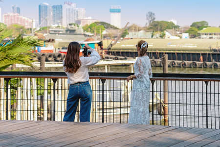 Back view portrait of attractive Asian women traveler take photo by digital camera together at riverside during weekend trip. Happiness and friendship of female friends. Attractions and travel conceptの写真素材