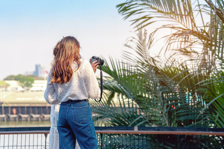 Back view portrait of attractive Asian women traveler take photo by digital camera together at riverside during weekend trip. Happiness and friendship of female friends. Attractions and travel conceptの写真素材