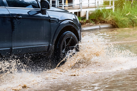 Car passing through a flooded road. Driving car on flooded road during flood caused by torrential rains. Flooded city road with a large puddle. Splash by car through flood water. Selective focus.の写真素材