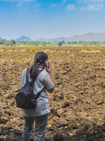 Back view of Asian backpacker woman use phone to talk business to plan farming in wilderness. Female...