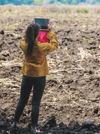 Female farmer use tablet to take wide angle shots of land to make farming decisions in soil field. Woman agriculturist use tablet photography to plan farming. Tablet imaging technology for cultivationの写真素材