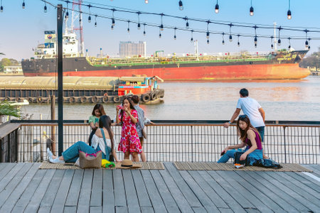 BANGKOK,THAILAND-FEBRUARY 23,2020 : Unidentified group of Asian friends or travelers using a smartphone or mobile phone take photo at riverside on sunny day during weekend trip at Hidden Woods.の写真素材