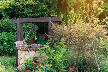 Beautiful artesian well made by stones and wheel pulley with metal bucket and rope in peaceful garden atmosphere. Retro stone water well in rural area. Garden decoration with antique items.の写真素材