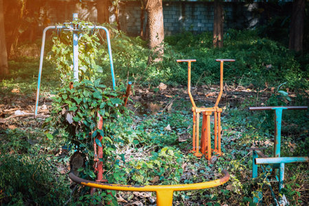 Old outdoor exercise equipment so worn out and covered in trees in outdoor exercise park. Old abandoned gym equipment on sports ground with overgrown grass. Unmaintained abandoned playground.の写真素材