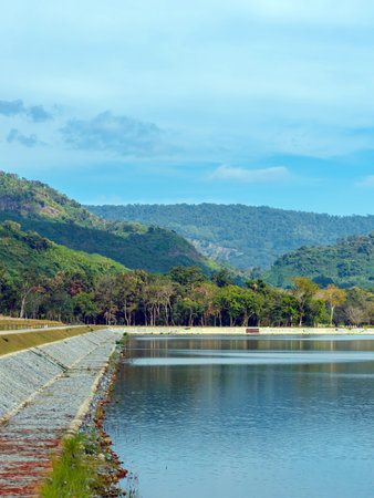 Beautiful and peaceful view of large reservoir with surrounding mountain and trees in beautiful sunshine and cloudy sky in Thailand. Tranquil and beautiful natural scenery landscape of reservoir lake.の写真素材