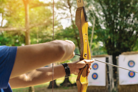 Hands of young man aims archery bow and arrow to colorful target in shooting range during training....