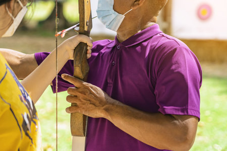 Young woman practice archery with male instructor closely supervising. Young female archer, young female archer, archery, shoot arrow with bow to target, archery training. Selective focus on hands.の写真素材