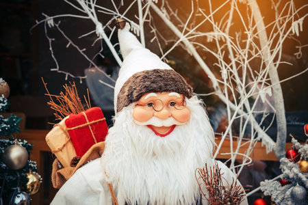 Cheerful Santa Claus model and Christmas tree with classic vintage decorations with garlands, lights, star dust and sparkles to celebrate New Year and Christmas display for celebration in public parkの写真素材