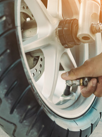 Hands of man check inflator pressure and inflates a tire on motorcycle with an air compressor. Man checking air pressure and filling the tire pressure on the motorbike wheel from automatic air filler.の写真素材