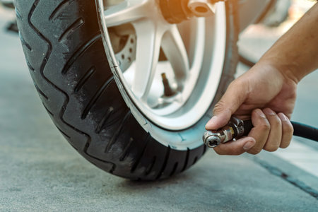 Hands of man check inflator pressure and inflates a tire on motorcycle with an air compressor. Man checking air pressure and filling the tire pressure on the motorbike wheel from automatic air filler.の写真素材