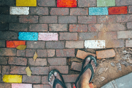 Feet of man wear sandals on old beautiful multicolor bricks paving stones footpath pattern on...