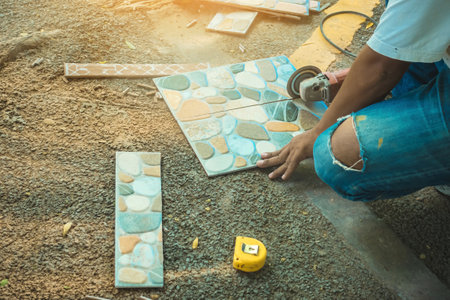 Hands of construction worker using an angle grinder for cutting the tiles at construction site. Man...
