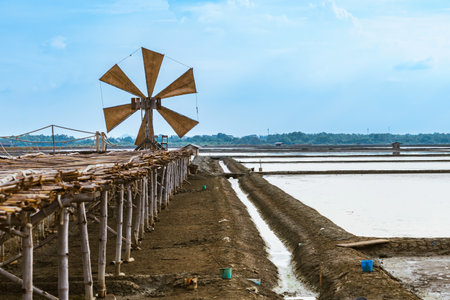 Wooden turbine at salt pan using for press seawater up to field with blue sky background in summer time of Thailand,South East Asia. Beautiful landscape of salt fields.Traditional salt farming cultureの写真素材