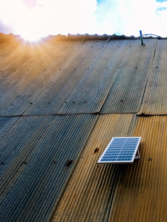 Solar panel attached on old zinc wall. Electric solar panel on the house wall. Small solar panel mounted on an outdoor galvanized wall with copy space. Using renewable solar energy technology concept.の写真素材
