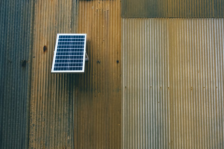 Solar panel attached on old zinc wall. Electric solar panel on the house wall. Small solar panel mounted on an outdoor galvanized wall with copy space. Using renewable solar energy technology concept.の写真素材