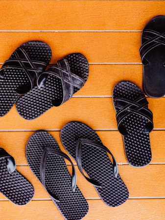 Top view of several pairs of classic black sandals on orange painted wooden background at the patio. Many pairs of rubber flip-flops next to open pool. Hygiene shoes rubber sandals of toilet room.の写真素材