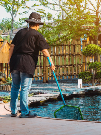 Back view of Asian woman in a black hat and black shirt wearing jeans using dip-net to scoop up...