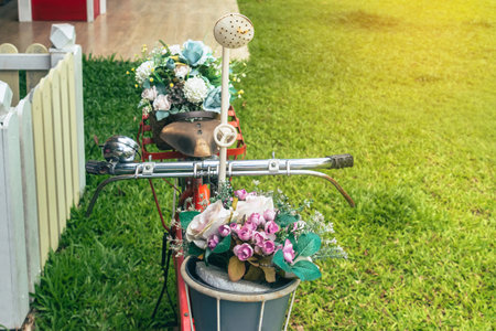 A beautiful bouquet of artificial plastic roses in bicycle front basket of old red bicycle in garden with green grass in background. Decoration artificial flower in basket on bicycle. Selective focus.の写真素材