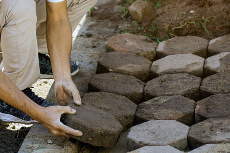 Hands of workman make it fit and to place stone pavers in a row. Construction site of pavement octagon bricks road. Installation or renovation repair. Lays out paving slabs. Selective focus on hands.の写真素材