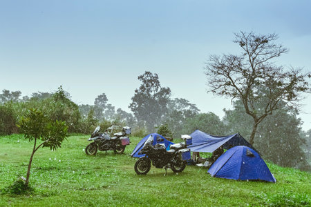 Motorcycle with rain. Camping activity in rain-filled holiday. Tent on campsite by the hill in rainy day. Mountain camp in forest in the rain. Motorcycle tourism in rainy season. Vacation destination.の写真素材