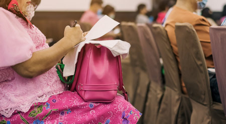 Hands of Senior woman wear face mask use pen to take notes of community meeting in auditorium....