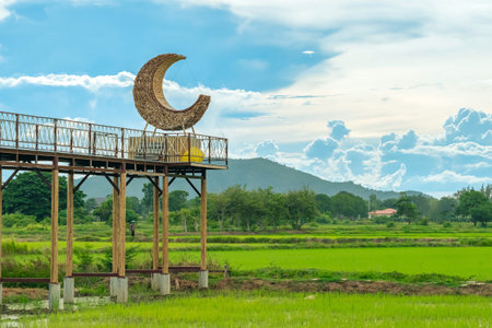 Beautiful crescent moon chair made of rattan for relaxation on bridge in paddy field with beautiful scenic in evening. Decorative wooden moon furniture as a sitting chair for viewpoint in rice field.の写真素材
