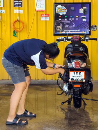 KANCHANABURI, THAILAND-NOVEMBER 21,2023 : Unidentified happy woman washing self-service her motorcycle at automatic coin-operated car wash machine. A vehicle in a coin-operated self-service car wash.のeditorial素材