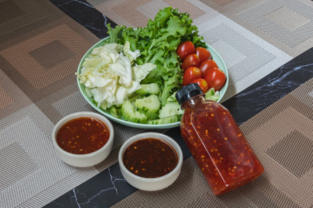 Fresh summer salad with early cabbage, cucumbers, tomato and lettuce in green plate with spicy sauce on brown placemat. Green vegetable salad in dish. Healthy fiber foods. Side dishes for Asian food.の写真素材