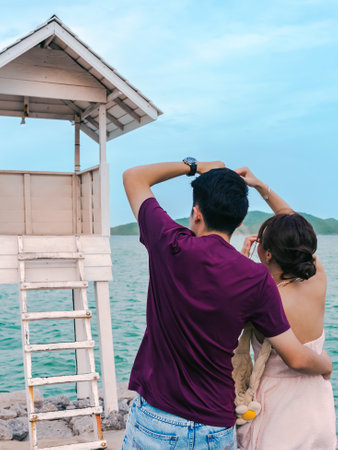 Happiness Asian lover with hands love sign on beach. Couple in love celebrates their engagement on seashore. Honeymoon trip. Lovers on beach. Wedding travel. Couple on vacation. Lover making heart.の写真素材