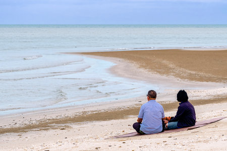 Asian mature couple in love sit to relaxing on beach travel summer holidays. Senior couple relaxing and spend time together at tropical beach., Healthy family lifestyle concept. Travel on vacation.の写真素材