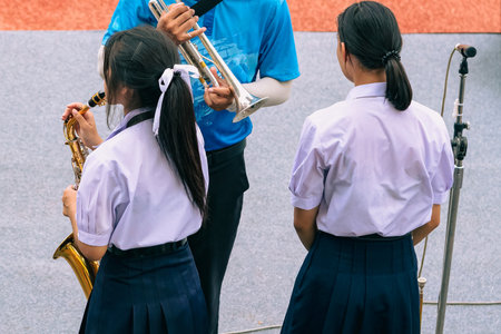 Group of Asian students in uniform perform a orchestra band in festival performance at stadium. Students play marching band in celebrations. Students Music band playing Jazz Music. Education outdoors.の写真素材