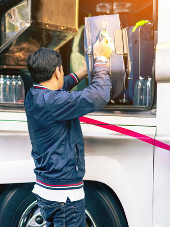 Tourists putting travel bag into travel bus at city street. Bus passengers putting luggage into the trunk when the bus stopped at terminal. Pack luggage and board the sightseeing bus. Happy journey.の写真素材