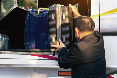 Tourists putting travel bag into travel bus at city street. Bus passengers putting luggage into the trunk when the bus stopped at terminal. Pack luggage and board the sightseeing bus. Happy journey.の写真素材