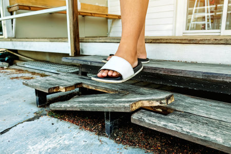 Feet of young woman wearing sandals walked down broken wooden stairs. Woman may be fell down stairs due to broken wooden leg stepladder. Ladder made of wood broke at home. Damaged wooden stepladder.の写真素材