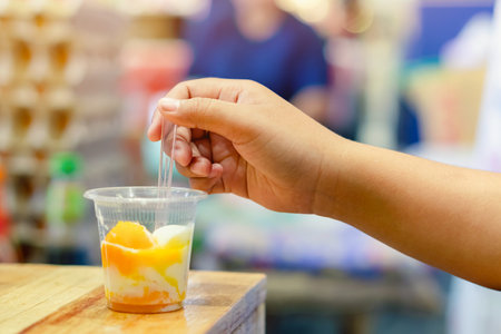 Hand of young woman eat delicious hard boiled eggs in plastic cup ready to eat. Breakfast with soft boiled egg in plastic cup served on wooden table. Traditional homemade simple food. Selective focus.の写真素材