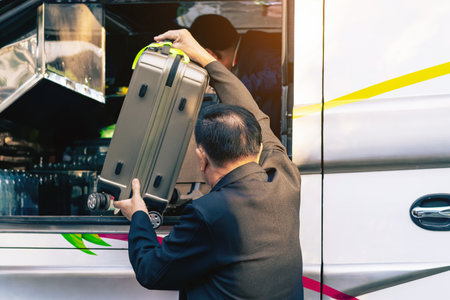 Tourists putting travel bag into travel bus at city street. Bus passengers putting luggage into the trunk when the bus stopped at terminal. Pack luggage and board the sightseeing bus. Happy journey.の写真素材