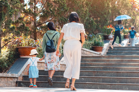 Back view of happiness woman in white clothes walking up stairs outdoors in park. Lady going up stairs in garden. Female tourist walking up stairs outside in park. Concept of casualness and leisure.の写真素材