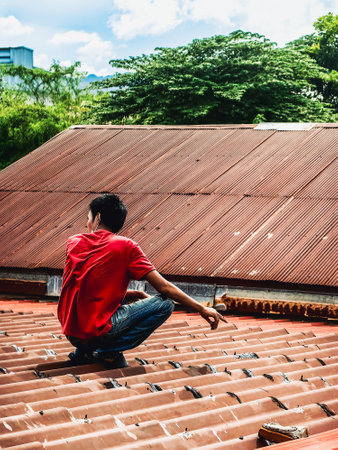 Technician man using polyurethane to seal leak on tiles roof. Man repaired roof by applying sealant to cover rain leaks. Worker man using waterproof roof coating repair to fix crack of old tile roof.の写真素材