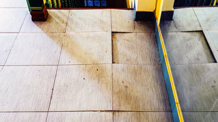 Background with falling off tiled tiles in living room. Close up of cracked ceramic tiles on a residential house floor surface due to improper construction material. Old tile floor cracked and broken.の写真素材