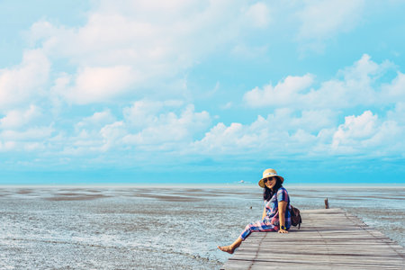 PHETCHABURI-THAILAND, JULY 25, 2020 : Unidentified happy Asian woman relaxing on tropical beach jetty (wooden pier) with low ocean tide in background at The King's Royally Initiated Laem Phak Bia.のeditorial素材