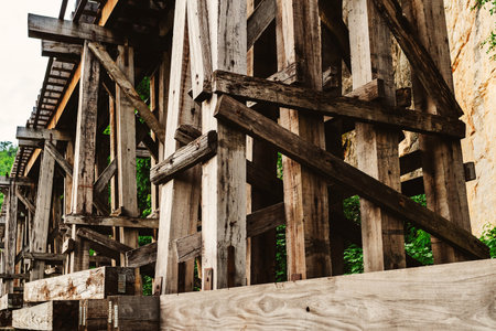 The ancient railway piers and large beams made of wood support an old rundown train bridge and were constructed during World War II.  View of old wooden bridge of train railway along cliffs and riversの写真素材