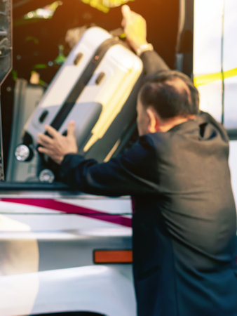Blurred image of senior male tourist putting travel bag into travel bus at city street. Bus passengers putting luggage into the trunk. Pack luggage and board the sightseeing bus. Elderly happy journey.の写真素材