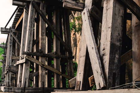 The ancient railway piers and large beams made of wood support an old rundown train bridge and were constructed during World War II.  View of old wooden bridge of train railway along cliffs and riversの写真素材