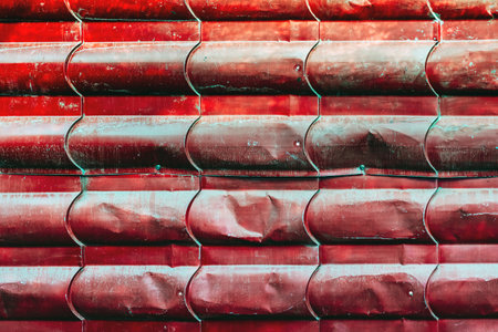 Artistic of old red metal tile fence background. Fence from corrugated board. Zinc metal sheet texture. Steel panel of enclosing wall. Old metallic sheet with peeling paint. Background or texture.の写真素材