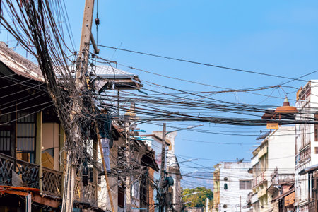 Electrician stand on ladder repairing the electrical system with tangle of wires in an old wooden village. technician working on ladder for maintenance wires attached to electric poles.の写真素材