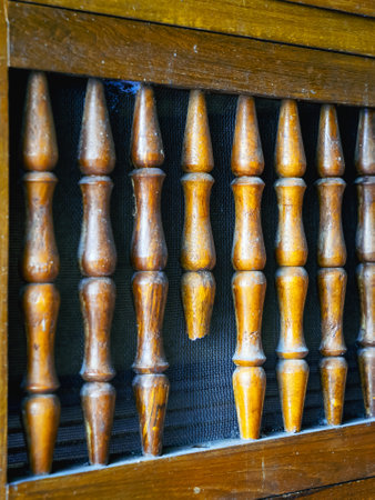 Old and broken lattice balustrade of wooden cupboard. Old broken railing of folding door with wire mesh in background of wooden cupboard or cabinet. Wooden railings broken and missing, leaving gaps.の写真素材